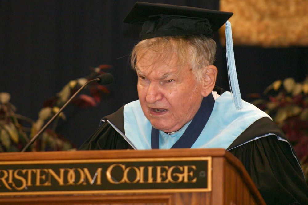 Man dressed in academic regalia stands at lectern that reads "Christendom College."