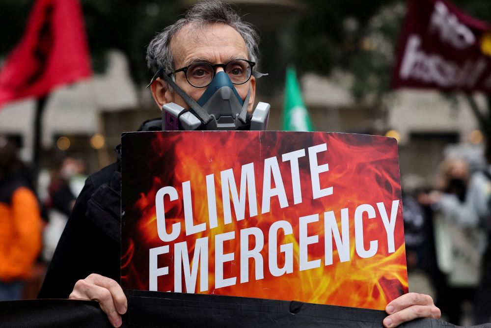 Man with mask holds sign that reads, "Climate Emergency."