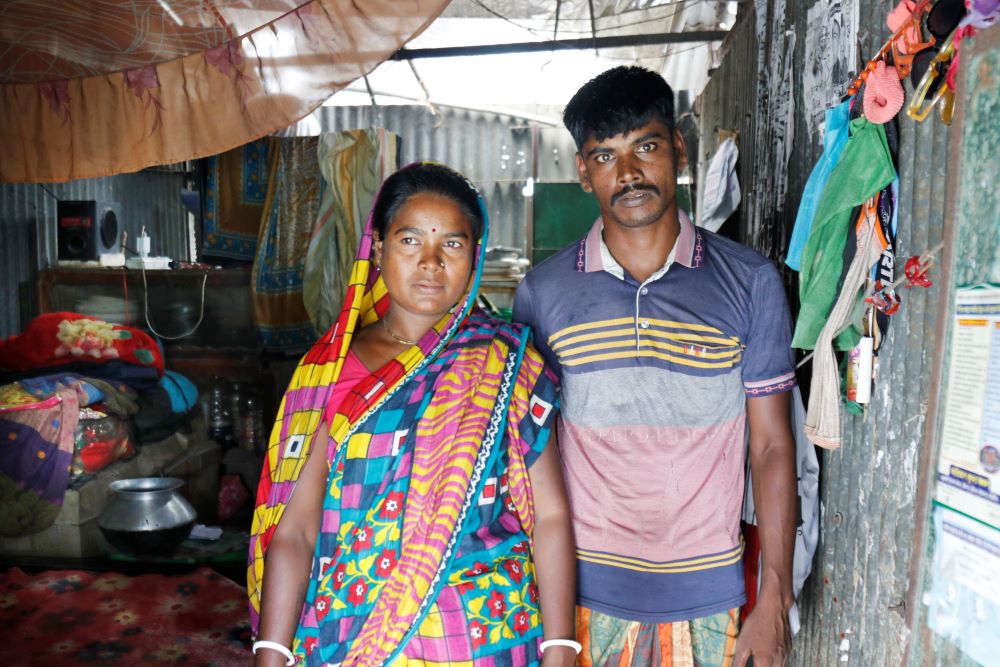 A man and woman stand together inside a simple home. 