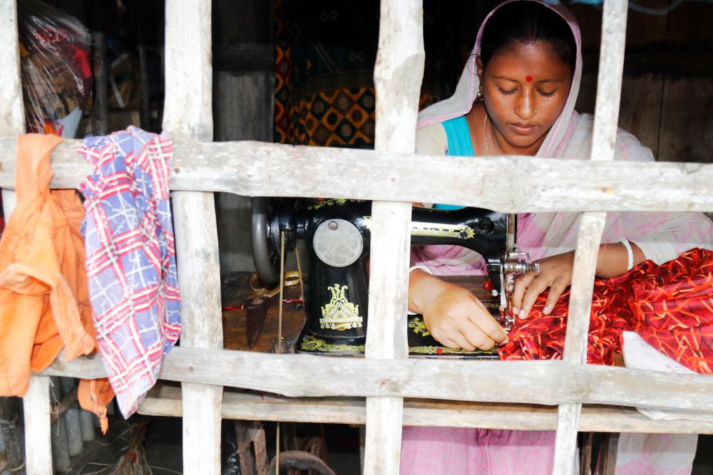 Woman works on a sewing machine in front of a window. 