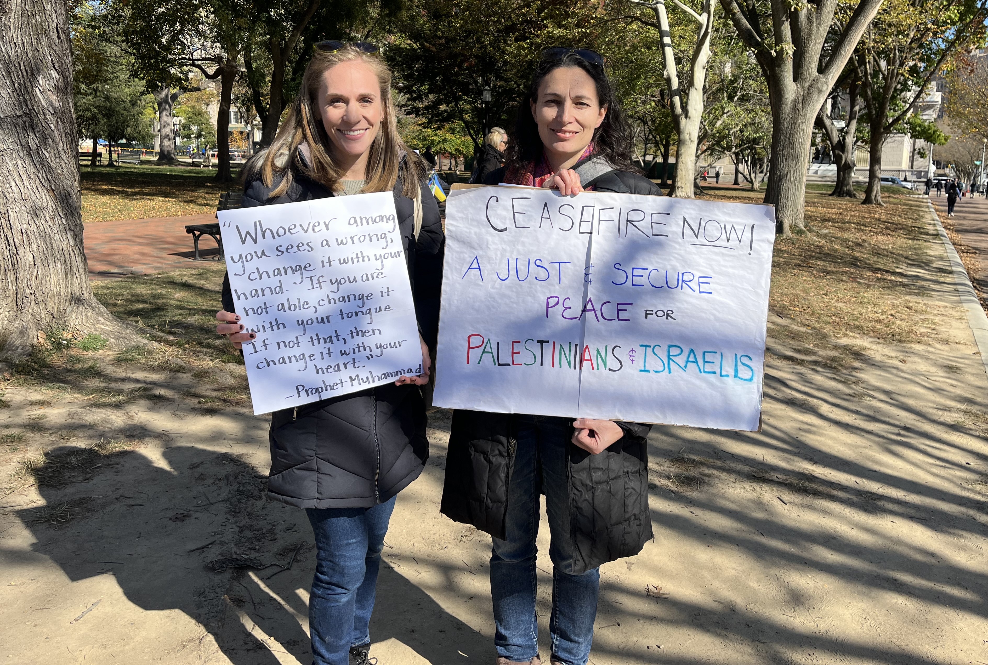Two women stand together, holding signs.