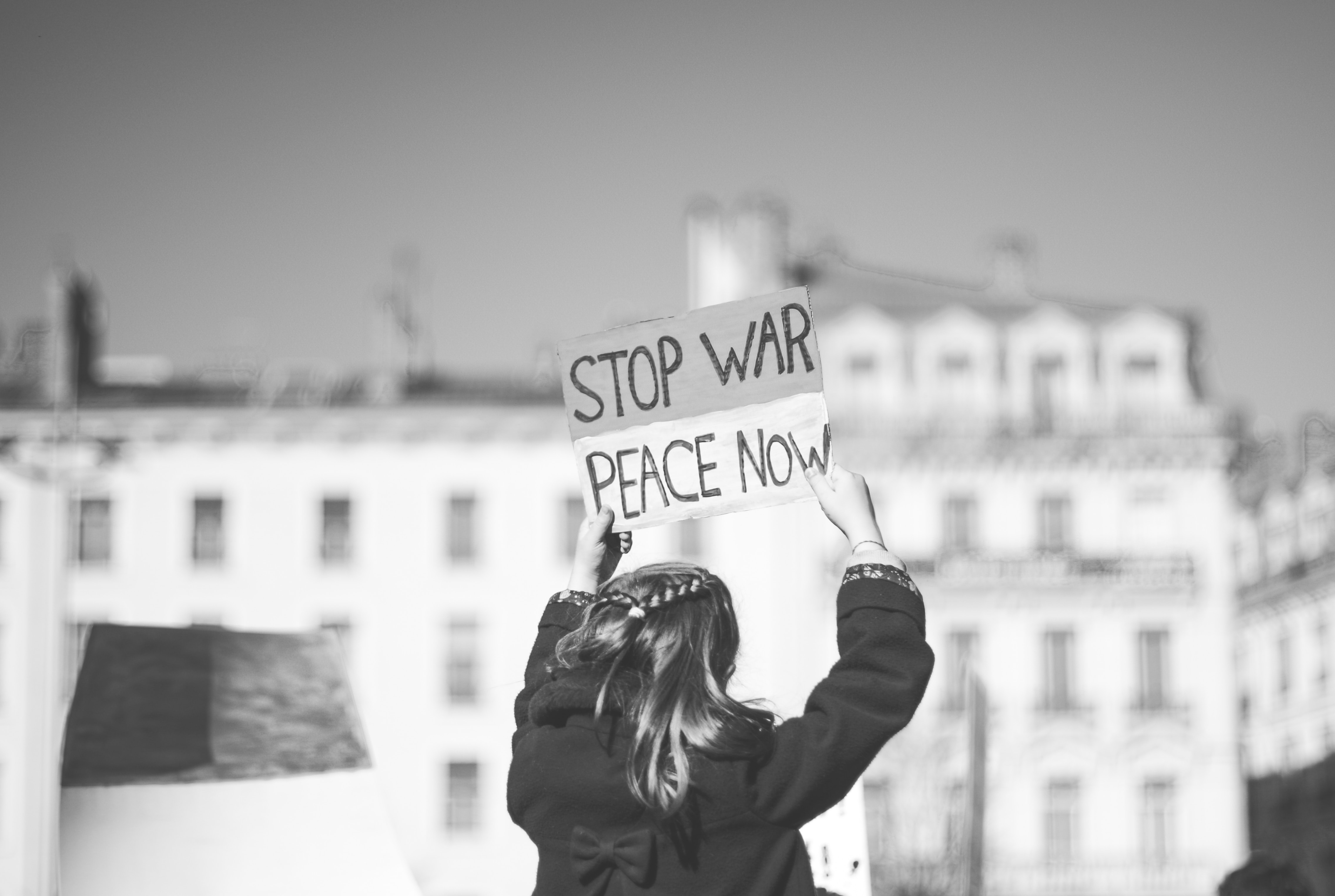 View from the back of a person holding a sign that says: "Stop war. peace now."