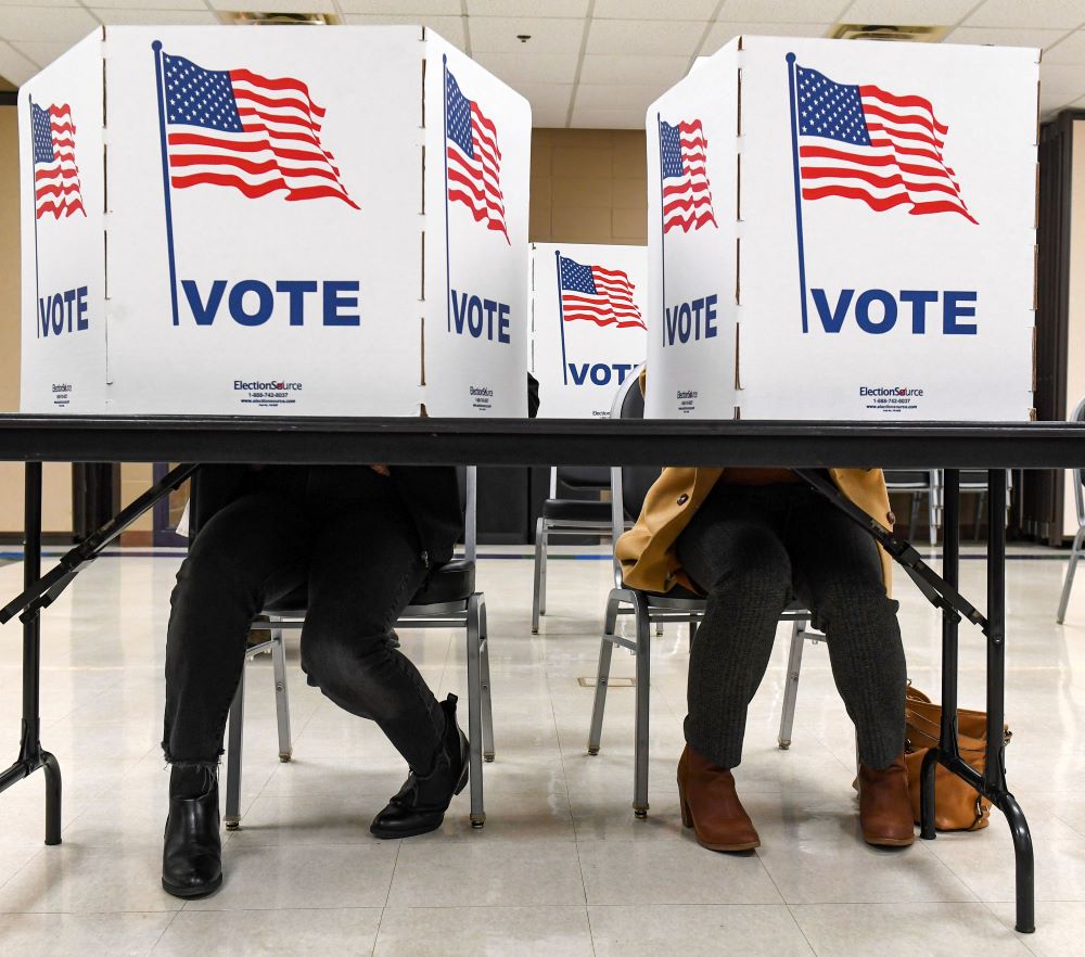 Voters fill out their ballots, sitting at a table and behind privacy screens made of signs with U.S flags and the word "vote."