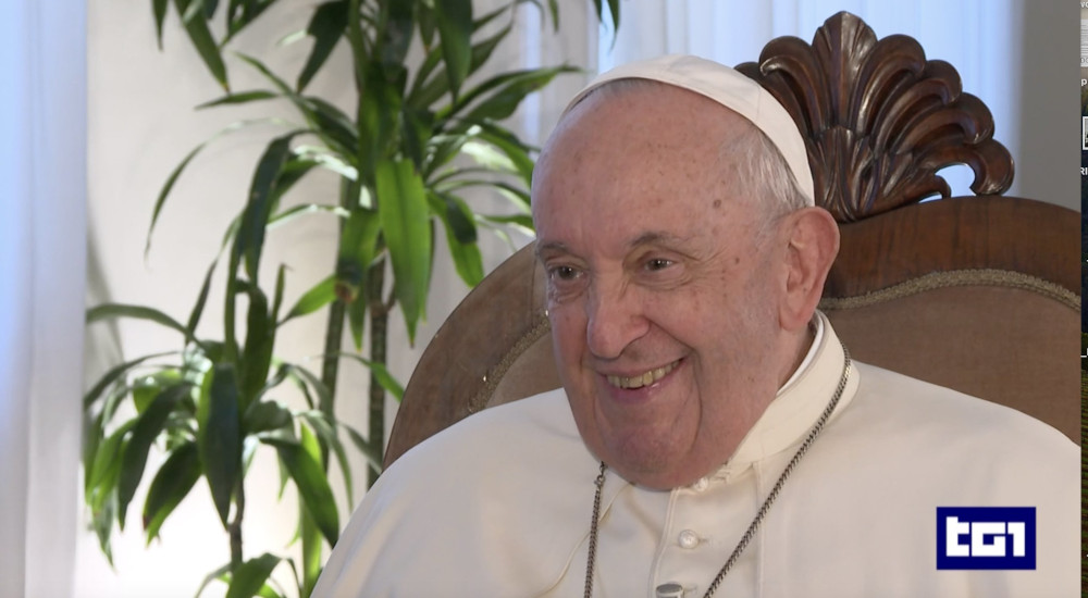 Pope Francis sits in a chair and smiles. A TG1 logo is at the bottom right of the screen.