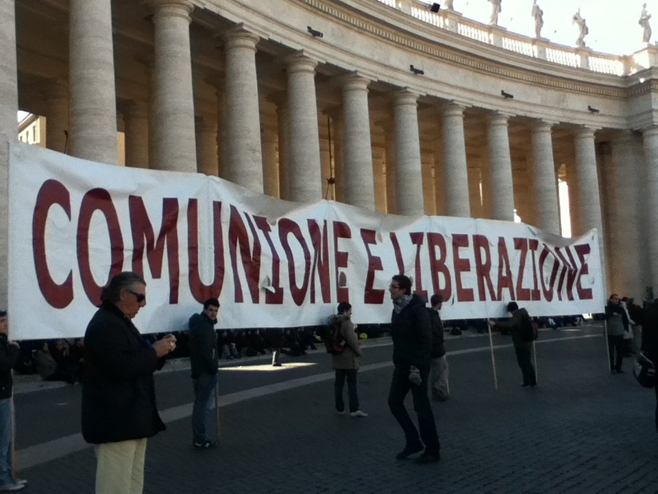People hold a banner that reads "Comunione e Liberazione" standing before the pillars in St. Peter's Square