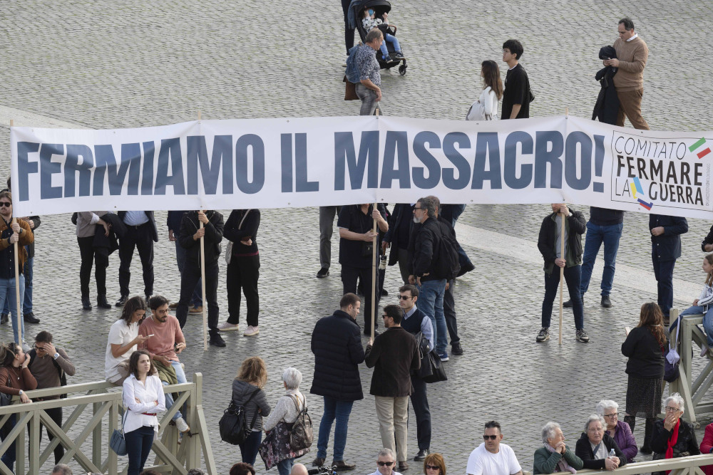 A group of people hold a long banner that says "Fermiamo il massacro" and "Comitato Fermare La Guerra"