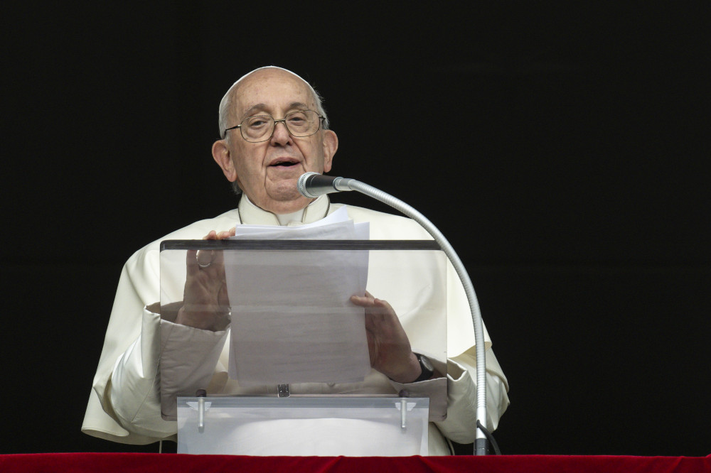 Pope Francis holds a sheet of paper and speaks into a microphone