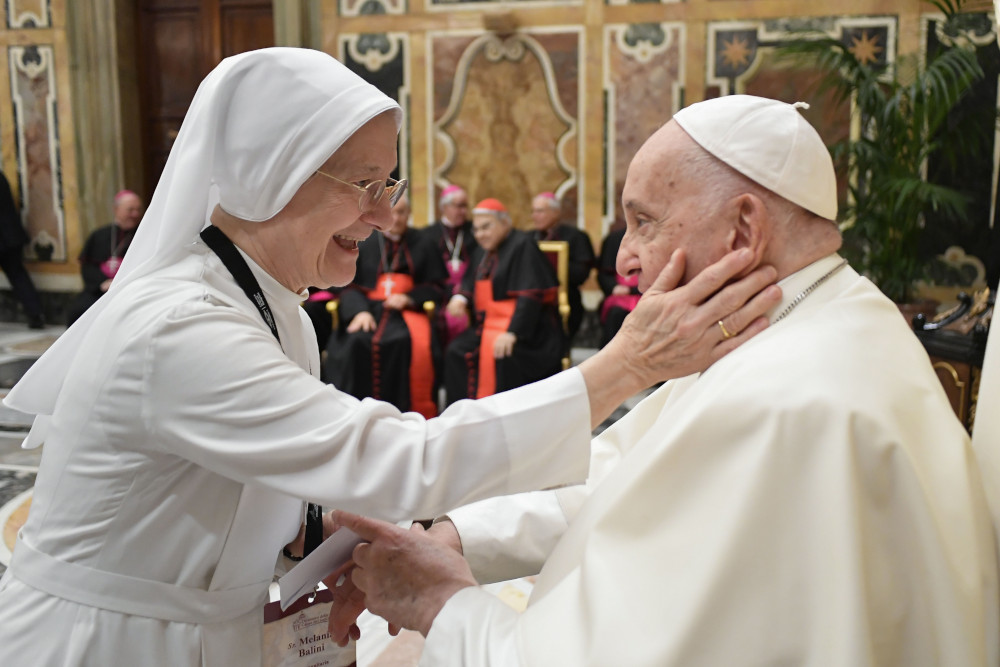 A woman religious wearing a white habit puts a hand on Pope Francis' cheek