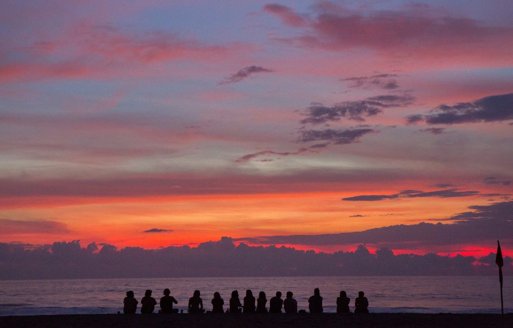 Silhouette of people in front of a lake and mountains at sunset. (Photo by Cristina Cerda/Unsplash/Creative Commons)