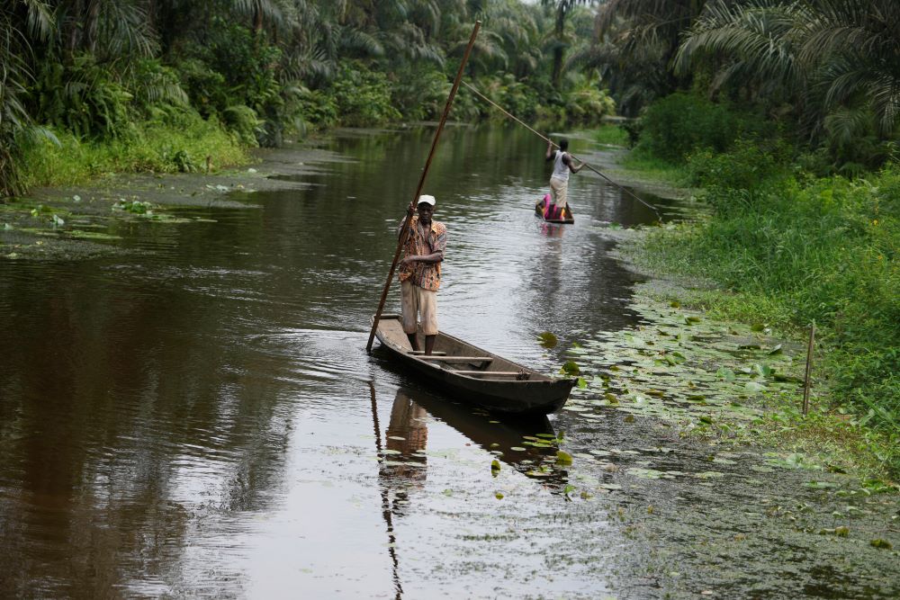 A man paddles a canoe near a Voodoo sacred forest in Adjarra, Benin, on Wednesday, Oct. 4, 2023. As the government grapples with preserving the forests while developing the country, Voodoo worshippers worry the loss of its spaces could have far reaching effects. (AP/Sunday Alamba)
