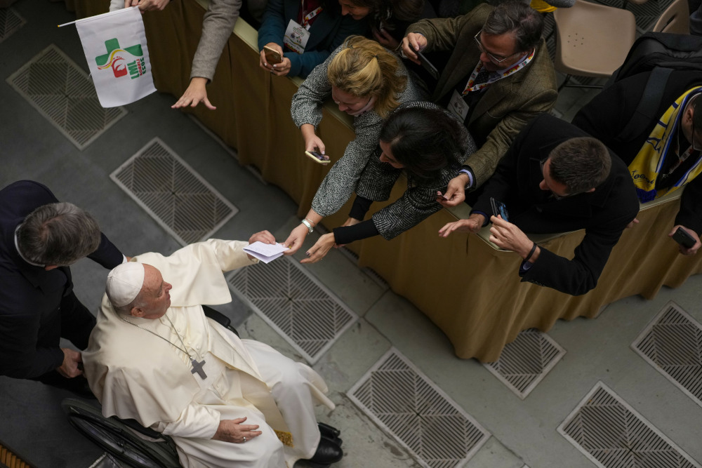 An overhead view of Pope Francis sitting in a wheelchair and shaking the hands of onlookers