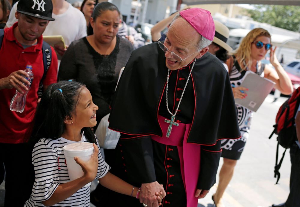 Bishop holds a little girls hand as they walk among a group.