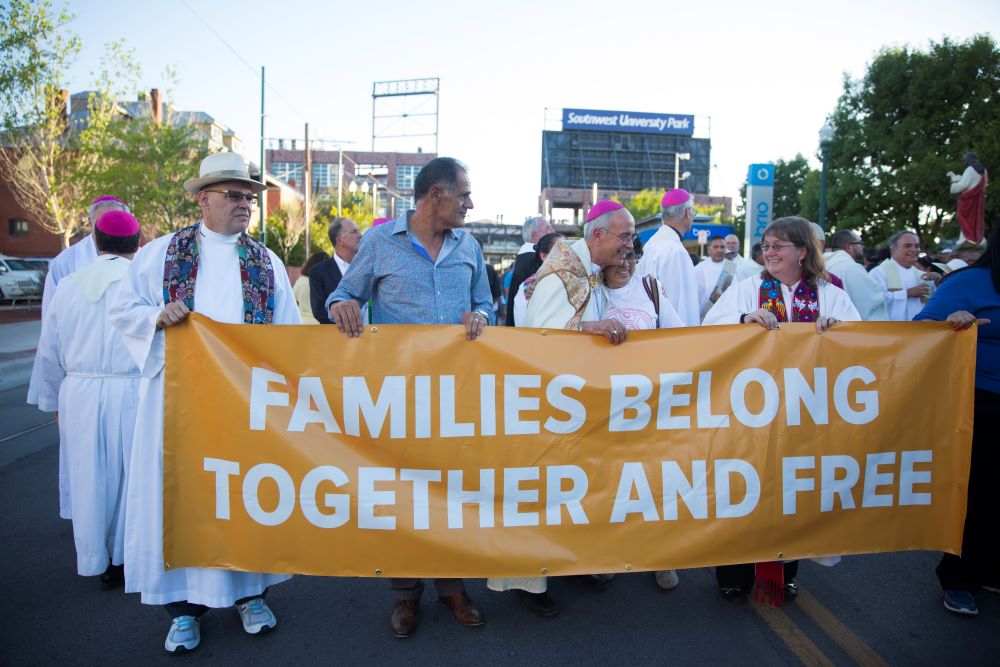 People hold banner reading, "Families belong together and free."