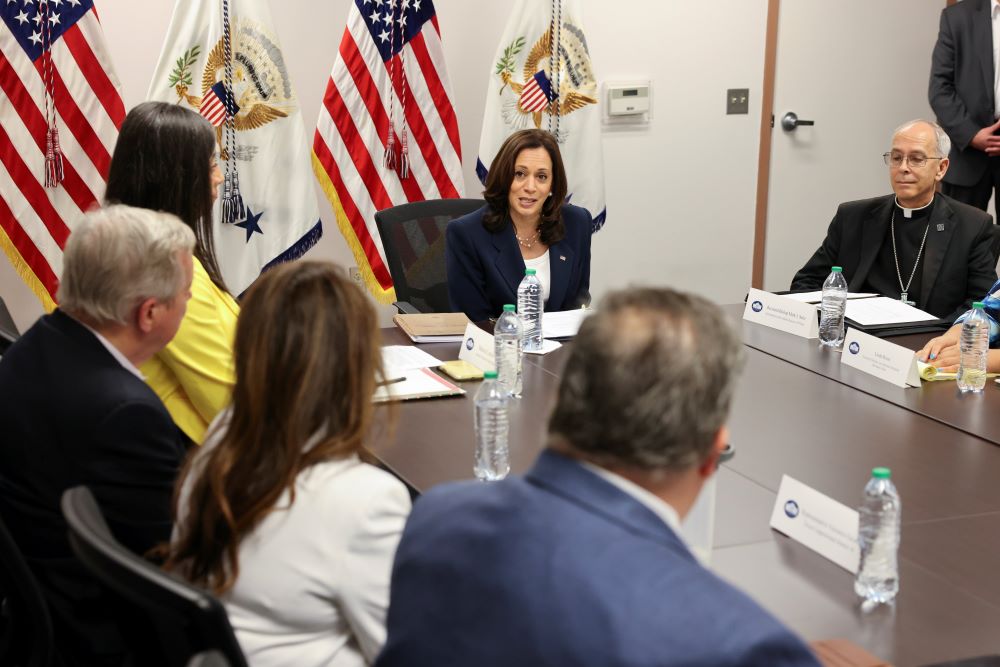 Several people sit at a table, including U.S. VP Kamala Harris and Bishop Mark Seitz.