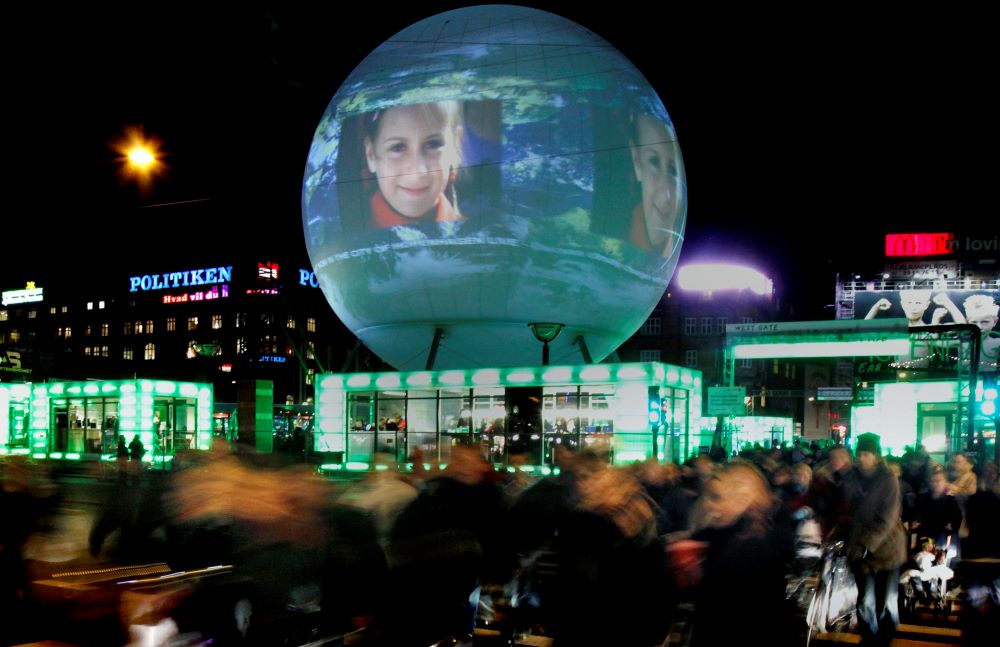 image with buildings with green lights in windows and a large globe-like item with images projected on it. 