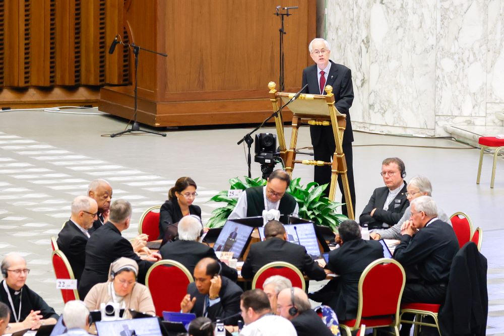 Man in suit talks to group at roundtables at synod. 