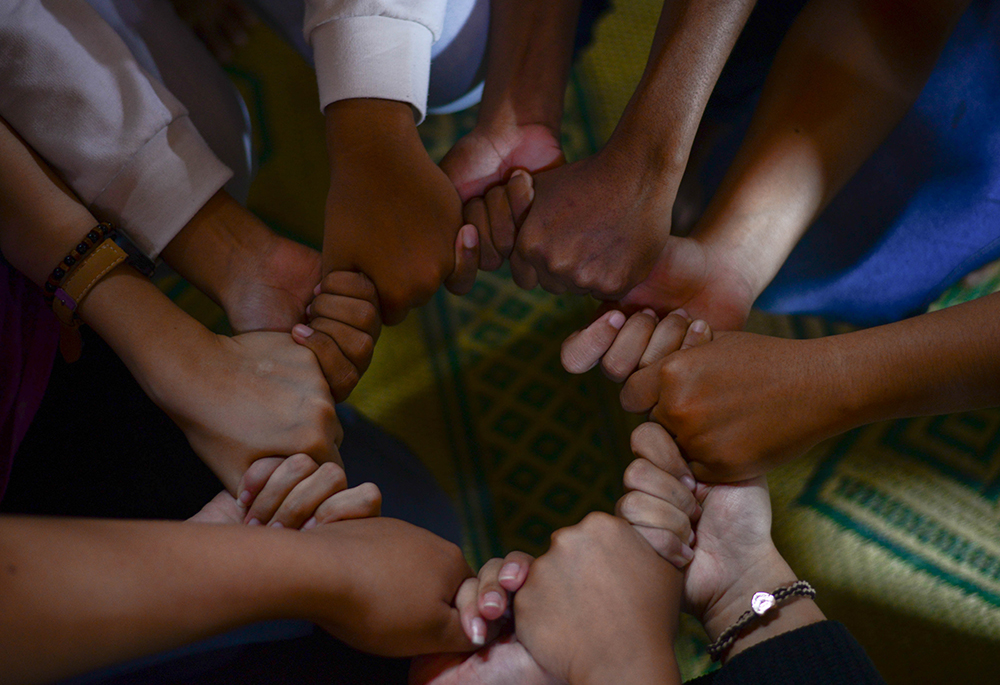 A photo illustration displays hands clasped together, forming a circle. (Unsplash/Wylly Suhendra)