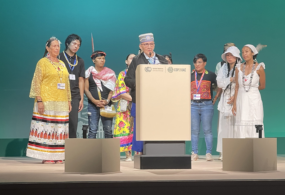 Indigenous people on stage during the People's Plenary Dec. 11 at COP28, the United Nations climate change conference, in Dubai, United Arab Emirates. At the microphone is Grandmother Mary Lyons, an Anishinaabe-Ojibwe Elder from Minnesota. (Courtesy of Catholic Relief Services)