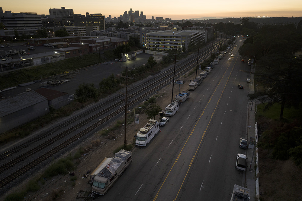 A line of weathered homeless RVs stretches along a street as the sun sets behind the Los Angeles skyline Sept. 18, 2023. (AP/Jae C. Hong)