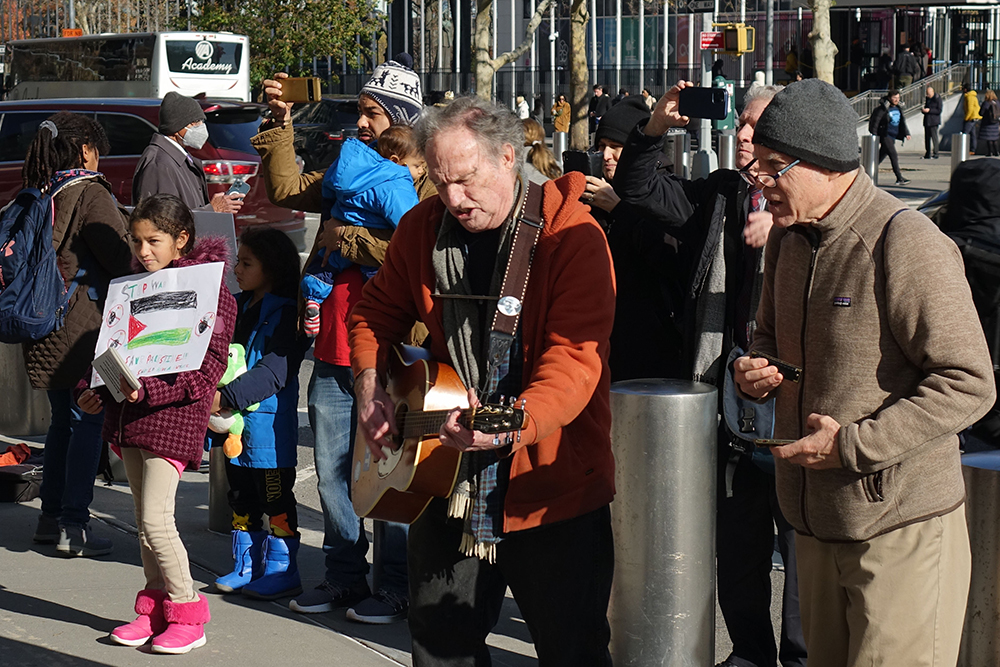 Bud Courtney, a member of the New York Catholic Worker, leads Catholic activists in song playing his guitar in front of the entrance to the United States Mission to the United Nations in New York City on Nov. 30. (Felton Davis)