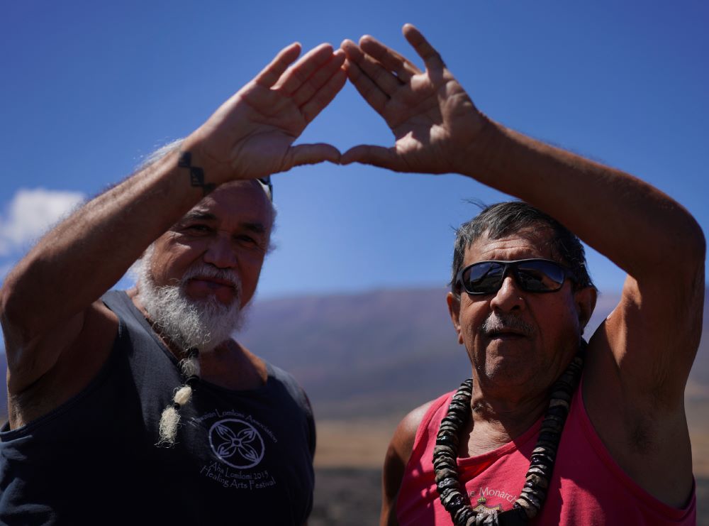 Elders Billy Keliiokalani Freitas, left, and Kini Palmyra Kaleilani in Mauna Kea, Hawaii on Saturday, July 15, 2023 put their hands together creating a symbol of support and solidarity for protecting Mauna Kea and for those blocking construction of a new telescope on the mountain. The symbol was birthed out of protests over the planned Thirty Meter Telescope. Freitas was one of the elders arrested during the 2019 protests. (AP Photo/Jessie Wardarski)
