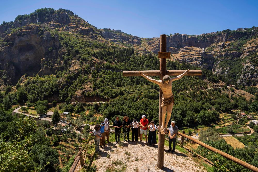 Lebanese priest Hani Tawk, center, prays with French tourists and his family next to a cross with a statue of a crucified Jesus Christ outside the Saint Elisha monastery in the Kadisha Valley, a holy site by Lebanon's Christians, in the northeast mountain town of Bcharre, Lebanon, Saturday, July 22, 2023. 