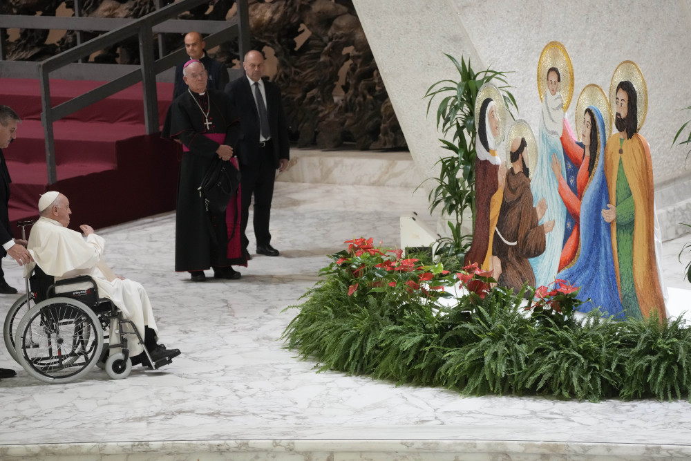 Pope Francis sits in a wheelchair before figures of the Holy Family and greenery