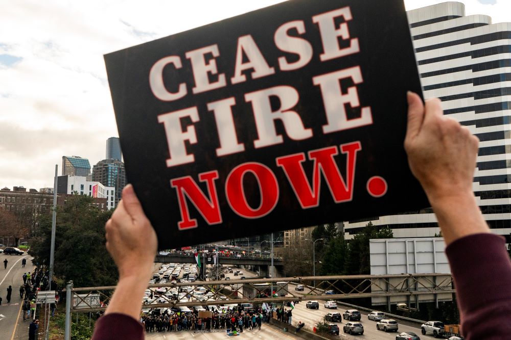 A protester holds a sign calling for a cease-fire to the Israel-Hamas war as others block Interstate 5 northbound on Jan. 6 in downtown Seattle. (AP/Lindsey Wasson)