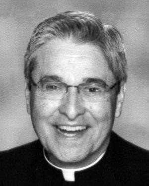 A black and white photo of an older priest wearing glasses and smiling broadly