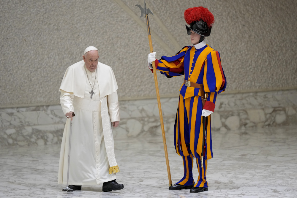 Pope Francis walks with a serious expression past a Swiss Guard wearing his colorful outfit