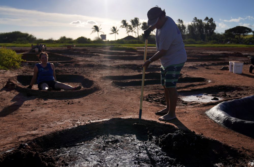 Roz Choi, left, and friend Eddie Topenio, tend to Choi's family salt beds on Sunday, July 9, 2023, in Hanapepe, Hawaii. The Choi family is one of 22 who over generations have dedicated themselves to the cultural and spiritual practice of "paakai," or Hawaiian salt. (AP Photo/Jessie Wardarski)