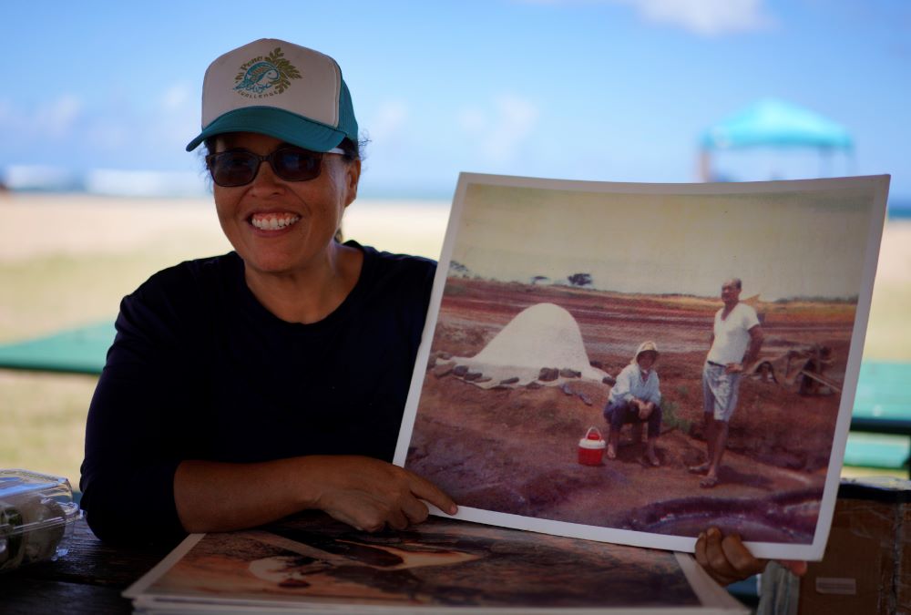 Malia Nobrega-Olivera shows a photo of her grandparents making Hawaiian salt, or "paakai," while sitting at Salt Pond Beach Park in Hanapepe, Hawaii on Sunday, July 10, 2023. (AP Photo/Jessie Wardarski)
