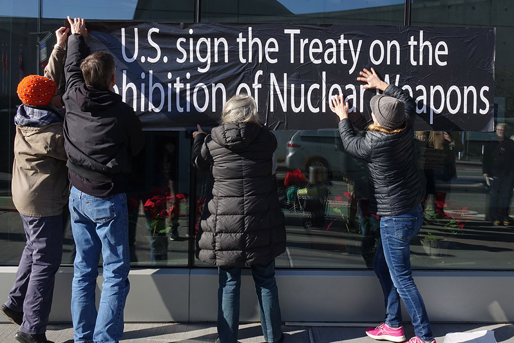 Catholic activists place large sticker posters on the walls of the United States Mission to the United Nations in New York City in 2023. The posters read, "U.S. sign the Treaty on the Prohibition of Nuclear Weapons." (Felton Davis)
