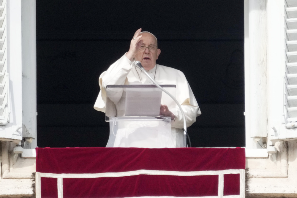 Pope Francis raises his right hand to make the sign of the cross from his apartment window