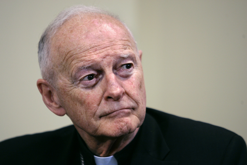 An older white man wearing a clerical collar looks off the camera with a serious expression