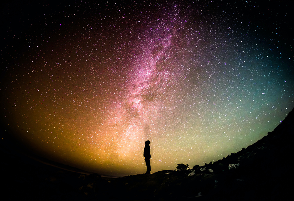 A photo illustration shows an outline of a person looking up toward a vast, colorful galaxy of stars.(Unsplash/Greg Rakozy)