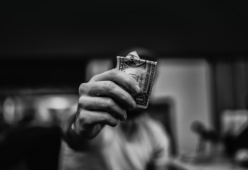A close-up of a hand holding out a folded dollar bill (Unsplash/Lucas Favre)