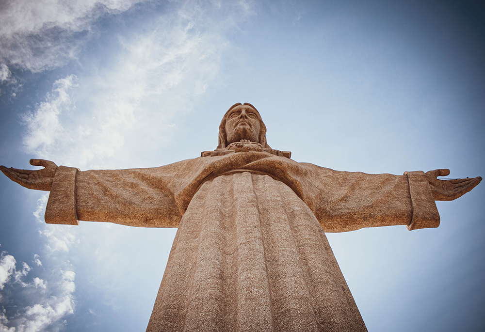 A large statue of Jesus is displayed in a photo taken from a low angle, displaying the statue in a dramatic angle against a blue sky. (Unsplash/Tim Hufner)