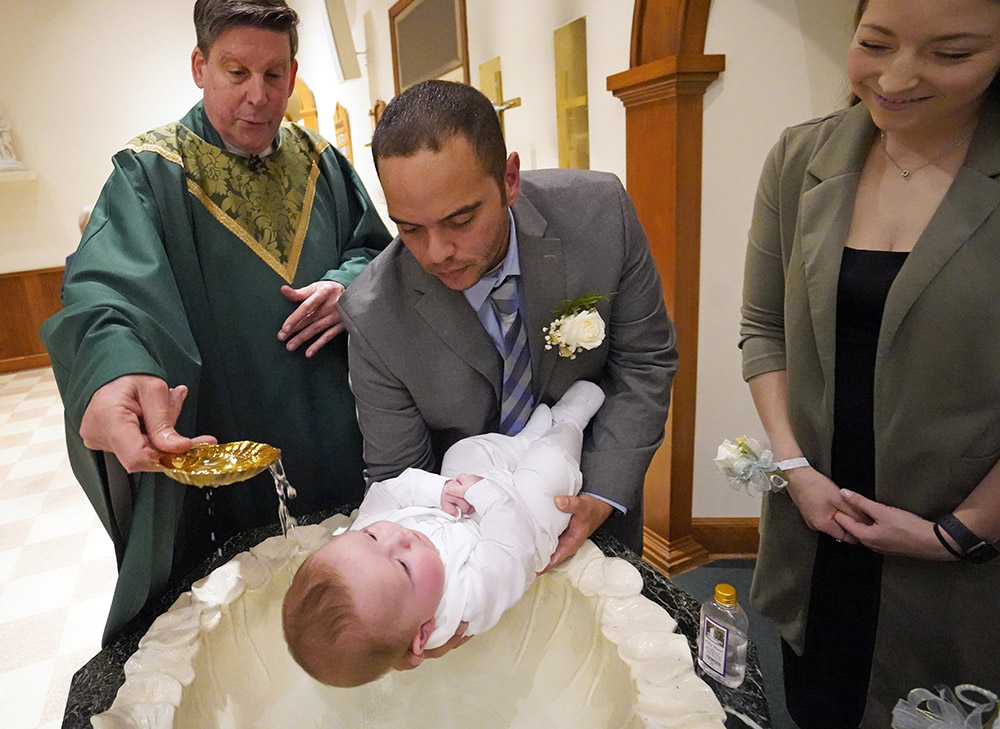 Julio Prendergast holds his 5-month-old son, Gabriel James, as he is baptized by Msgr. Frank Schneider Nov. 12, 2022, at St. John the Baptist Church in Wading River, New York. Looking on is the baby's mother, Christina Prendergast. (OSV News/Gregory A. Shemitz)