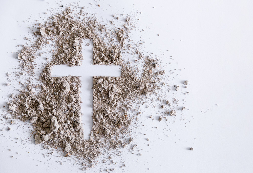 Cross traced in a pile of ash on a white surface (Dreamstime/Thai Noipho)