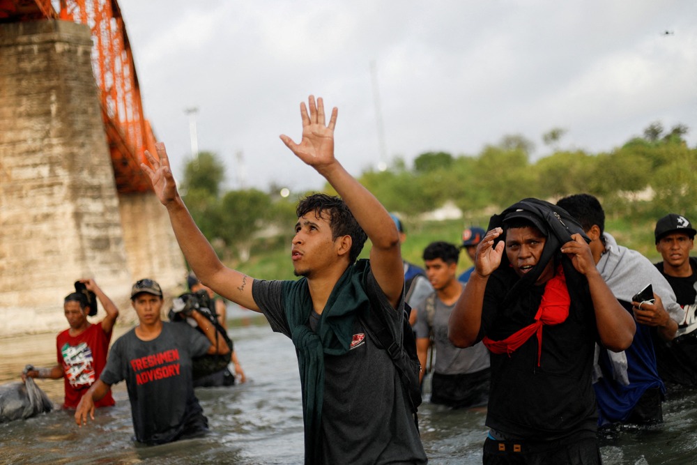 Venezuelan migrants cross U.S-Mexico border Young man wading through water with his hands up