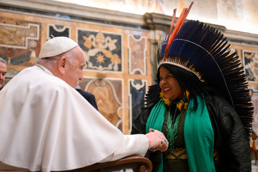 Pope Francis shakes hands with indigenous woman wearing head dress
