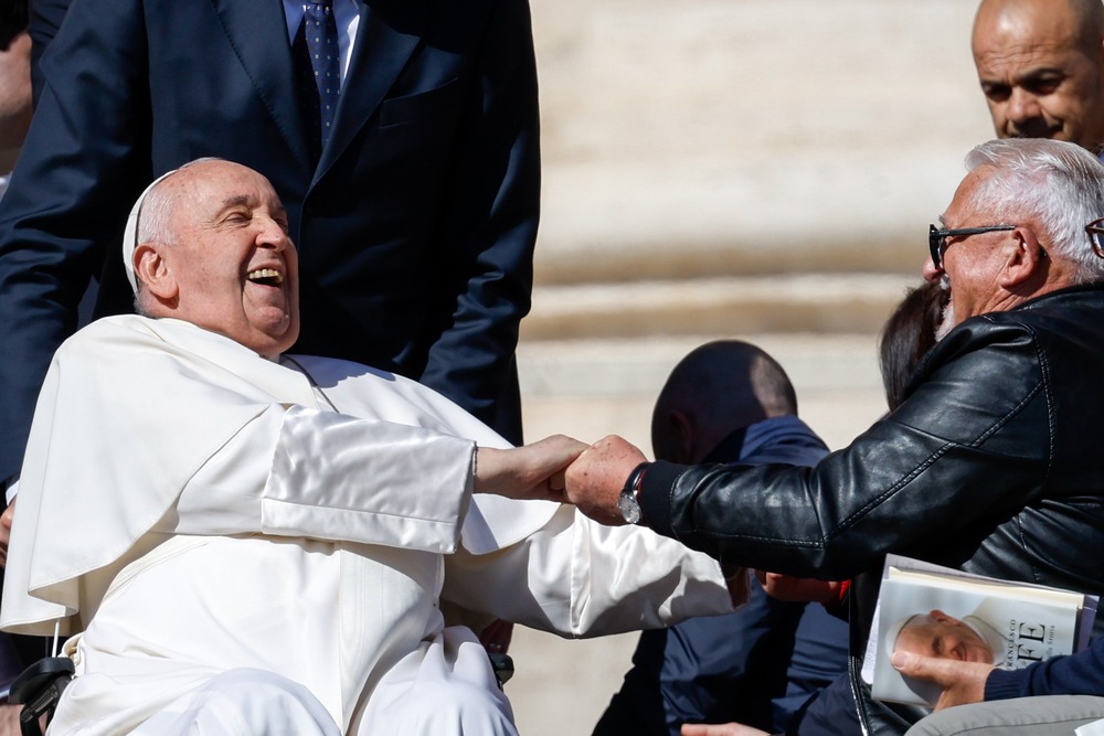 Pope Francis throws head back, laughing and gripping hand of guest