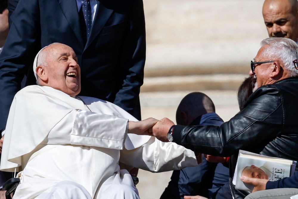 Pope Francis laughs during general audience Pope Francis throws head back, laughing and gripping hand of guest