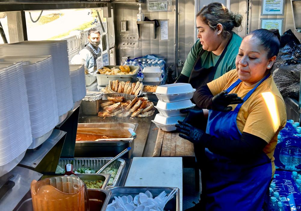 Marisol Ortiz Perez, right, and Araceli Orta prepare meals Feed My Poor distributes to unhoused people near LA's MacArthur Park. The nonprofit distributes about 300 meals there on Tuesdays, Thursdays and Saturdays.