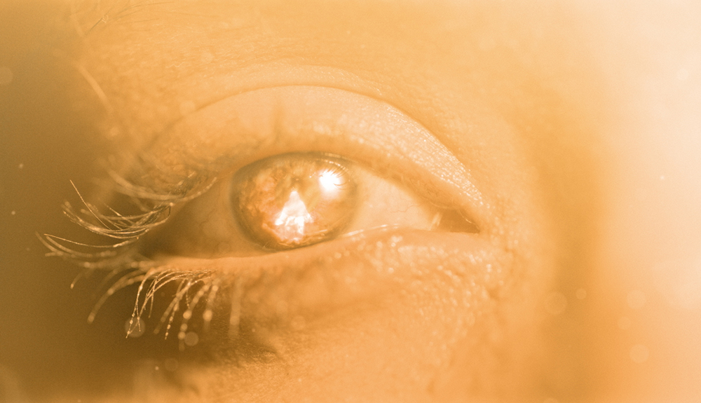 A still from the movie "After Death" shows a closeup of an eye bathed in bright, warm light. A reflection of a brilliant shape is shown reflected in the center of the eye. (Courtesy of Angel Studios)