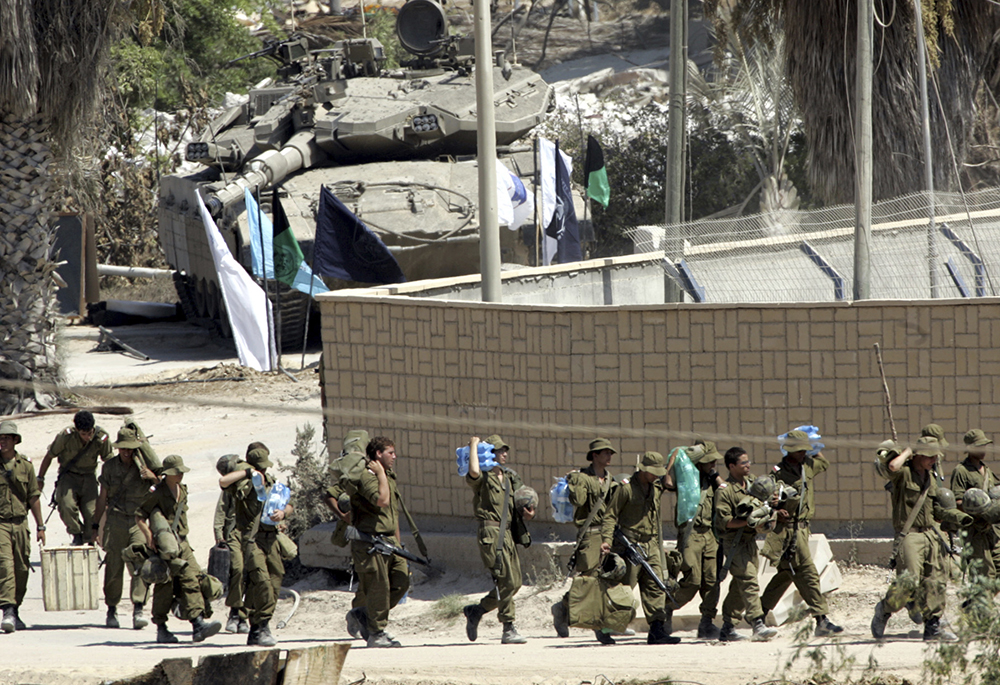 Israeli soldiers carry their equipment as they prepare to leave the Israeli settlement of Kfar Darom in the central Gaza Strip, Sept. 11, 2005. In 2005, in the wake of a second and far more violent intifada, or uprising against Israeli occupation, Israel withdrew its soldiers and over 8,000 settlers from Gaza. (AP photo/Pier Paolo Cito, File)