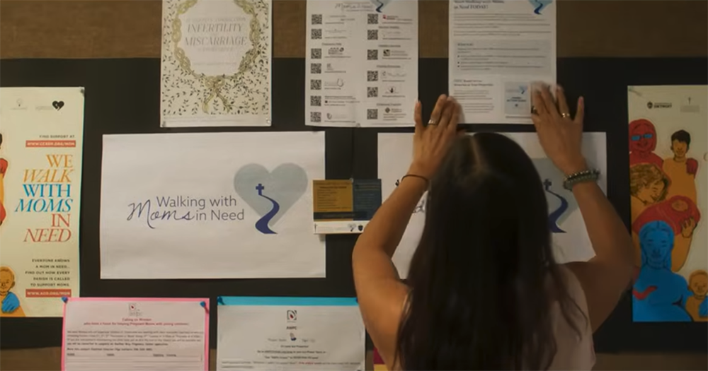A woman hangs up informational flyers in this screengrab of a video from the U.S. bishops' conference about the Walking with Moms in Need initiative. (NCR screengrab/YouTube/USCCB Secretariat of Pro-Life Activities)
