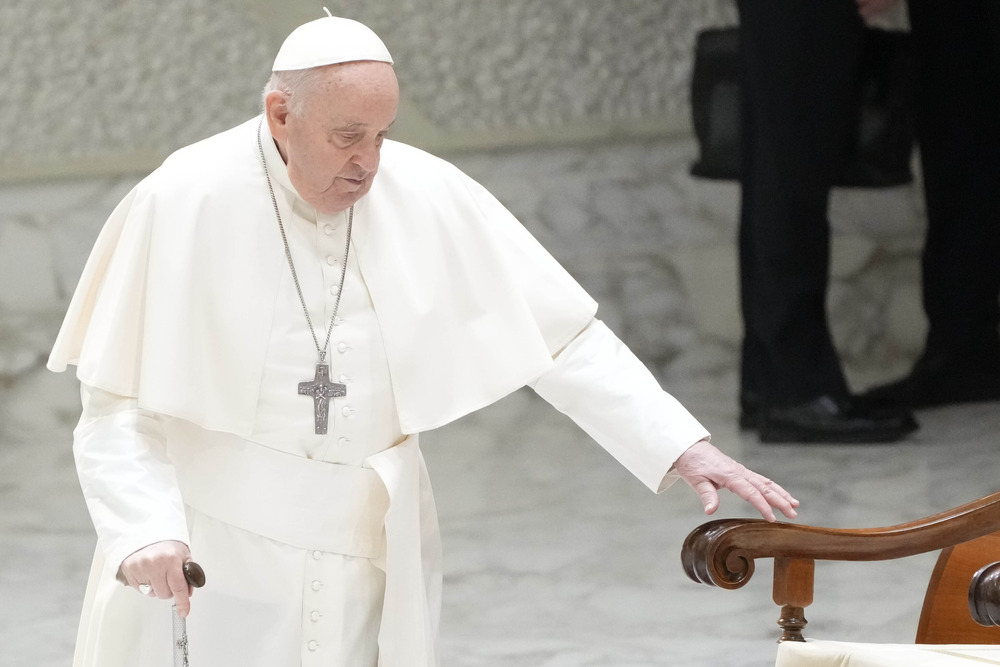 Pope Francis walks with cane towards chair. 