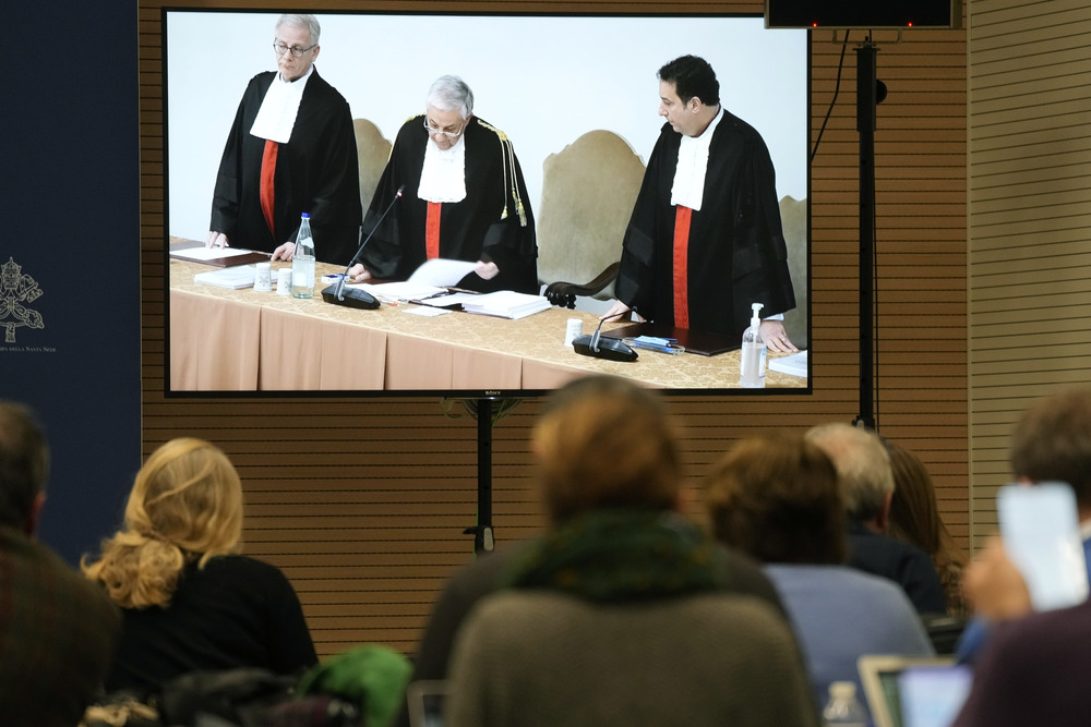 Reporters watch a screen in the Vatican press room showing Vatican tribunal president Giuseppe Pignatone reading the verdict of a trial against Cardinal Angelo Becciu and nine other defendants. 